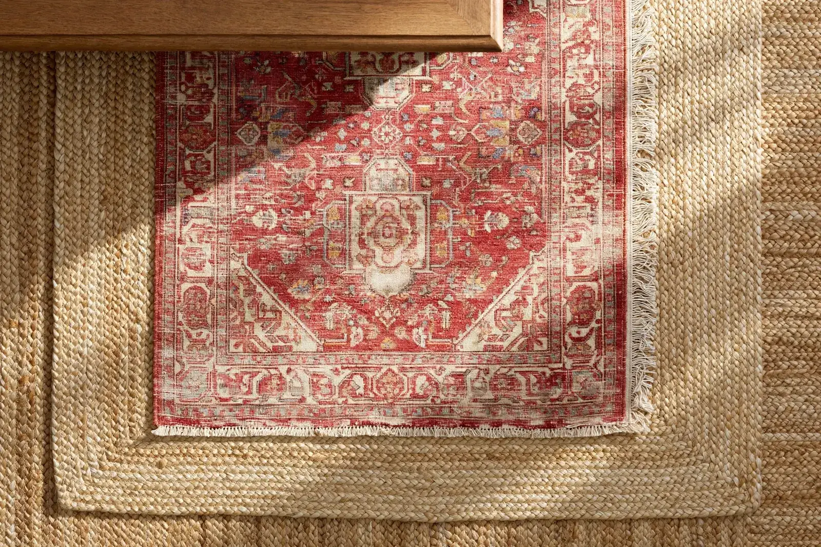 Close-up of layered rugs in a living room, showing a patterned top rug over a natural base rug